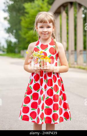 Jeune heureux enfant d'âge scolaire élémentaire, fille gaie tenant un bouquet de fleurs de champ, bouquet d'herbes, souriant, à l'extérieur, une personne,dre colorée Banque D'Images