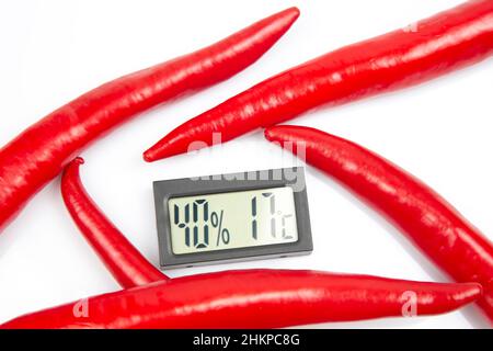 thermomètre numérique pour mesurer la température et l'humidité de l'air sur fond de poivrons rouges. métaphore du piment Banque D'Images