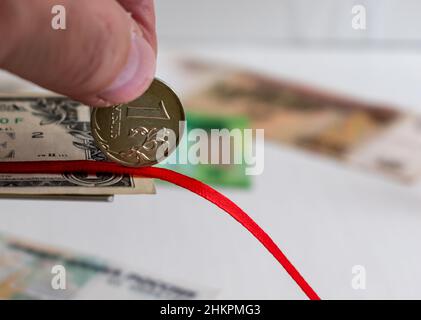 Une pièce rouble sur ruban rouge incliné gros plan à la main sur fond flou Banque D'Images