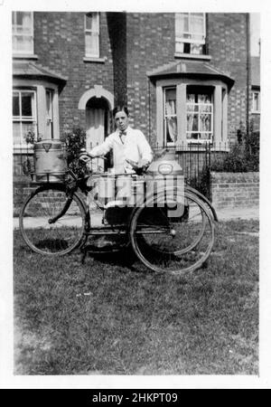 Garçon de lait portant un manteau blanc et un noeud papillon, délivrant du lait et de la crème sur un tricycle. Banque D'Images