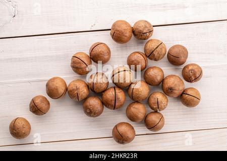 Plusieurs noix de macadamia brunes mûres, gros plan, sur une table en bois, vue du dessus. Banque D'Images