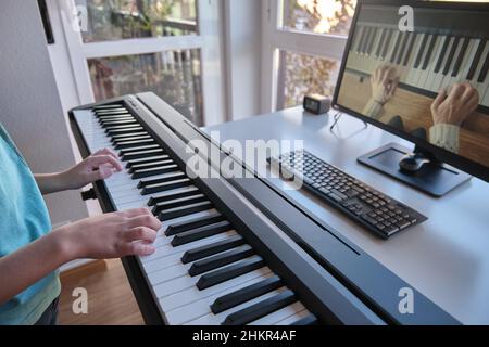 Garçon regardant le piano tutoriel vidéo avec ordinateur.Personne pratiquant le jeu avec une leçon et un cours en ligne.Classe Internet pour apprendre un nouvel instrument. Banque D'Images