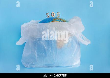 Globe terrestre dans un sac en plastique et inscription SOS, fond bleu.Concept - écologie, pollution de la planète avec du plastique cellophane polyéthylène jour de la Terre, W Banque D'Images