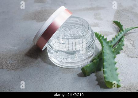 Texture de gel avec des bulles d'acide hyaluronique et des branches d'aloe vera dans un pot de verre sur un fond de béton Banque D'Images