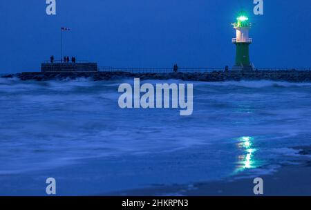 05 février 2022, Mecklembourg-Poméranie occidentale, Warnemünde : le phare de l'une des jetées à l'entrée du canal maritime de Rostock clignote dans la soirée.Le temps sec et froid de l'hiver attire encore les vacanciers et les visiteurs de jour à la plage même après le coucher du soleil, malgré le vent féroce.Photo: Jens Büttner/dpa-Zentralbild/dpa Banque D'Images