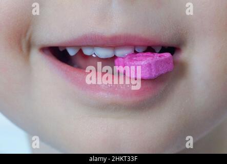 L'enfant heureux sourit et tient une vitamine rose dans sa bouche.Concept de nutrition et de soins de santé pour les enfants et les bébés.Gros plan Banque D'Images