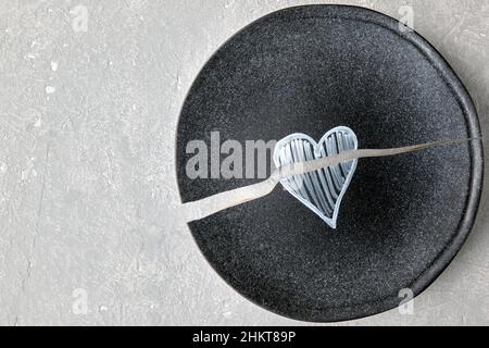 Une plaque en céramique cassée avec un coeur peint sur une table en béton léger Banque D'Images