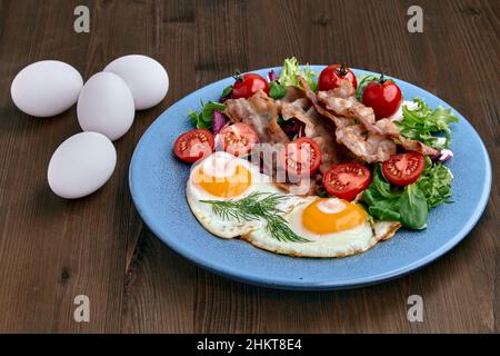 Œufs frits avec bacon, laitue et tomates cerises sur une assiette bleue Banque D'Images