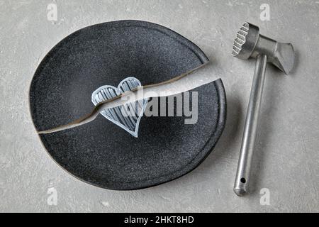 Plaque de céramique cassée avec un coeur peint et un marteau de cuisine Banque D'Images