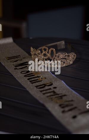 Photo sombre d'un tiara d'anniversaire avec le numéro 80 et une ceinture d'anniversaire sur une table en bois Banque D'Images