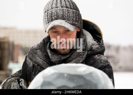 Un sculpteur sculpta une boule de glace ronde sur un bloc de glace avec un burin. Banque D'Images