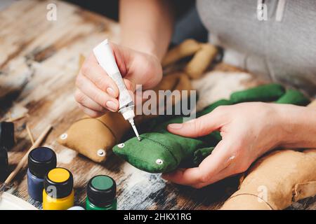 Grenouille poupée douce à la main.Bricolage fabrication de cadeaux.Les mains humaines tiennent le jouet mou grenouille.Accessoires pour travaux d'aiguille sur fond gris.Décoration maison faite à la main.Processus de Banque D'Images