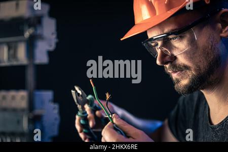 Un électricien mâle travaille dans un tableau de commutation avec un câble de connexion électrique. Banque D'Images