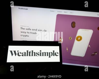 Personne tenant un téléphone cellulaire avec le logo de la société canadienne de services financiers Wealthsimple à l'écran devant la page Web. Mise au point sur l'affichage du téléphone. Banque D'Images