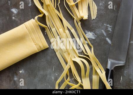 Pâte, rayures crues de nouilles et couteau de cuisine sur la surface en poudre de farine en bois Banque D'Images