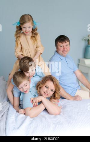 Famille joyeuse jouant ensemble sur le lit.Les parents passent leur temps libre avec leur fille et leurs deux fils.Grande famille caucasienne jouant à la maison dans la chambre.Maman et papa se trompent avec les enfants Banque D'Images