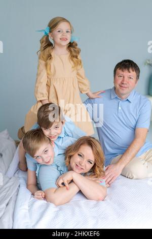 Famille joyeuse jouant ensemble sur le lit.Les parents passent leur temps libre avec leur fille et leurs deux fils.Grande famille caucasienne jouant à la maison dans la chambre.Maman et papa se trompent avec les enfants Banque D'Images