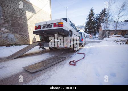 L'ancienne voiture est chargée sur une remorque et remorquée pour entretien.Voiture chargée sur remorque en temps de witer.Assistance technique sur la route dans un village. Banque D'Images