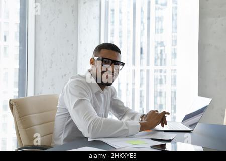 Joyeux employé du millénaire noir en lunettes, tenue de coffrage travaillant sur le projet Banque D'Images