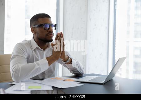 Paisible et sérieux, jeune homme d'affaires afro-américain méditant, priant sur le lieu de travail Banque D'Images
