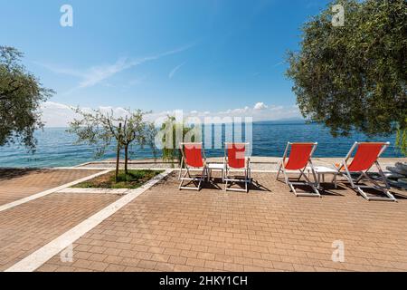 Chaises longues orange vides sur une belle plage sur le lac de Garde (Lago di Garda) entre le petit village de Bardolino et la ville de Garda. Vénétie, Italie. Banque D'Images