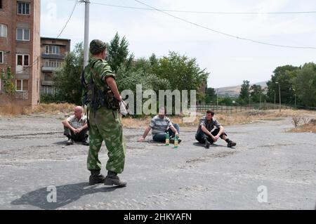 Des civils géorgiens détenus sont assis sur le terrain tandis que des soldats russes foutent leurs maisons pour trouver des armes dans la ville de Gori, peu après que les forces russes sont entrées dans la ville pendant la guerre russo-géorgienne d'août 2008 Banque D'Images