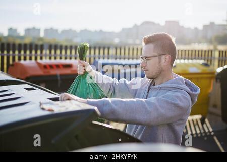 Homme marchant avec des ordures.Personne jetant le sac en plastique vert à la poubelle sur la rue de la ville. Banque D'Images