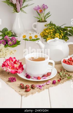 Tisane à la rosehip, camomille et limbes dans une tasse blanche sur une table blanche en bois avec des fleurs. Banque D'Images