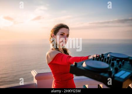 Les femmes du DJ jouent de la musique en mélangeant et en grattant le soir avec fond de mer et doux coucher de soleil chaud.Gros plan d'une console DJ contrôlée par Banque D'Images