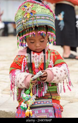 Une jeune fille, portant des vêtements traditionnels de la tribu Hmong, recueille de l'argent pour poser pour des photos par des touristes à Sapa (sa Pa), Lao Cai, Vietnam Banque D'Images