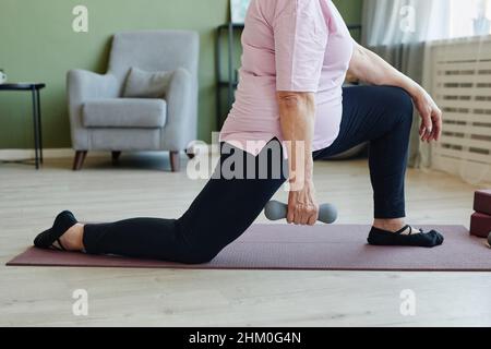 Partie inférieure de la femme active senior tenant une haltère pendant l'exercice physique sur le tapis de yoga sur le sol de la salle de séjour à loisir Banque D'Images