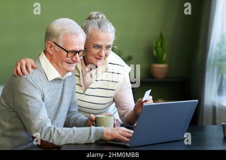 Un mari et une femme heureux regardant l'écran d'ordinateur portable tout en commandant des plats à emporter ou d'autres produits dans la boutique en ligne Banque D'Images