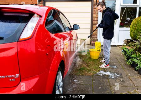 Woodbridge, Suffolk, Royaume-Uni février 24 2021: Un jeune homme à pression lave sa voiture propre Banque D'Images