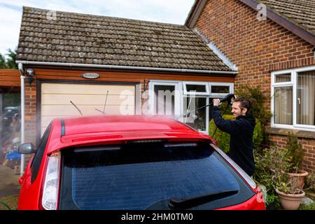 Woodbridge, Suffolk, Royaume-Uni février 24 2021: Un jeune homme à pression lave sa voiture propre Banque D'Images