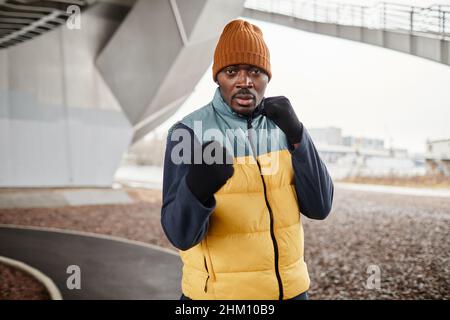 Attrayant et en forme de jeune sportif afro-américain pratiquant l'exercice de boxe pendant l'entraînement physique en plein air le matin Banque D'Images
