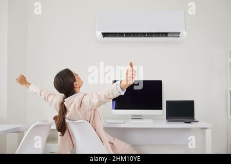 Une femme heureuse se détendant à son bureau sous l'air frais et frais qui coule de la climatisation Banque D'Images