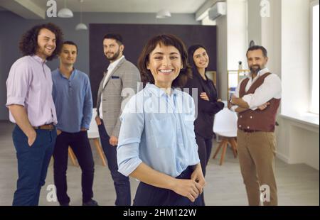 Femme d'affaires souriante et confiante au bureau avec ses collègues en arrière-plan Banque D'Images