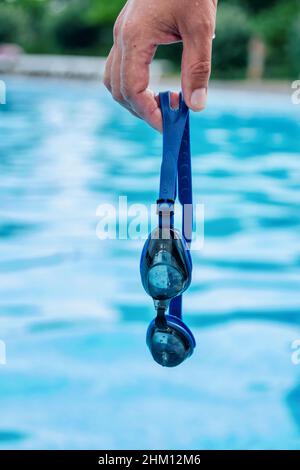 Main de l'homme tenant des lunettes de natation professionnelles avec de l'eau bleu de piscine sur fond Banque D'Images