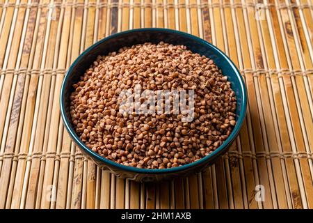 Gruaux de sarrasin biologique cru dans un bol bleu sur un tapis de table en bois.Grains de sarrasin de wholegrain torréfiés pour un régime sans gluten et des concepts de fibres alimentaires Banque D'Images