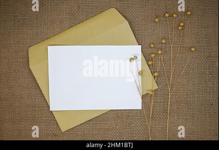Maquette avec enveloppe et carte vierge. Une enveloppe en papier kraft sur toile de jute. Fleurs séchées (lin sec avec gousses de graines) à côté de l'enveloppe. Banque D'Images