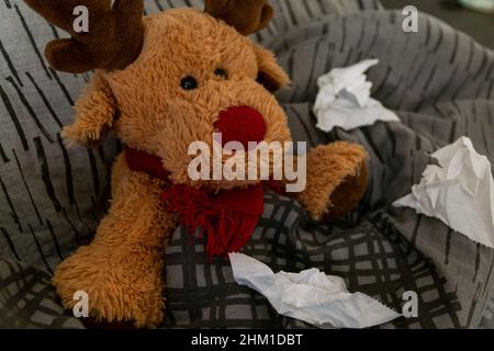 Un adorable ours en peluche renne niché dans le lit avec un rhume, une grippe, un covid, une maladie avec un rouleau de papier toilette utilisé autour de la couverture.Combattre la maladie à la maison Banque D'Images