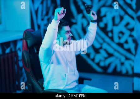 Jeune gars joue sur la console de jeu avec manette de jeu assise sur la chaise appréciant la victoire gagner. Banque D'Images