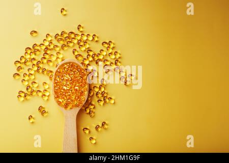 Capsules de vitamine D3 dans une cuillère avec d'autres capsules de vitamine D3 autour d'elles sur fond jaune. Anciennes capsules avec un supplément alimentaire pour les articulations te Banque D'Images