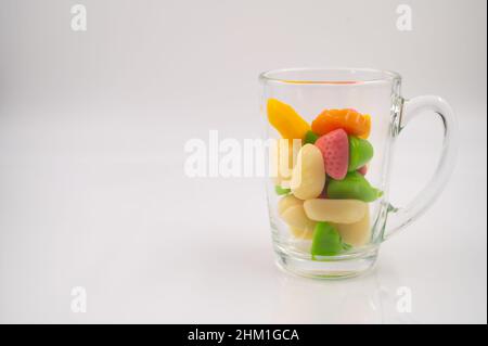 Bonbons en gelée colorés dans une tasse en verre transparent sur un fond blanc isolé.Copier l'espace. Banque D'Images