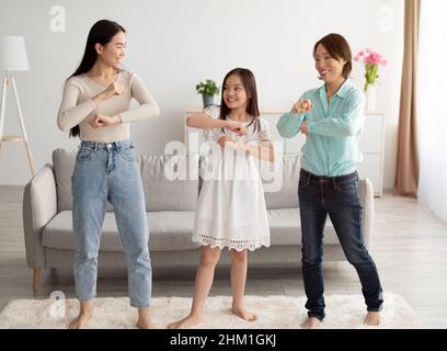 Bonne petite fille asiatique avec sa mère et sa grand-mère dansant, s'amusant à la maison Banque D'Images