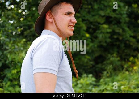 Homme en chapeau.Portrait d'un fermier souriant avec de l'herbe verte et de la nature des arbres en arrière-plan.Jeune homme portant un chapeau de cow-boy sur le terrain.Gros plan.Joyeux jeune p Banque D'Images