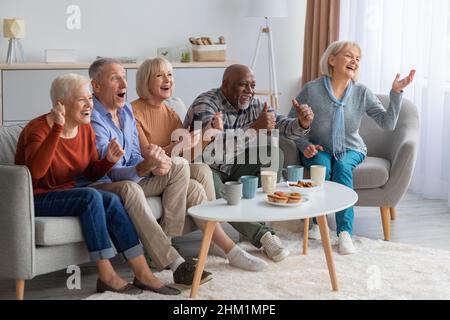 Des personnes âgées émotionnelles regardant la télévision dans le salon Banque D'Images