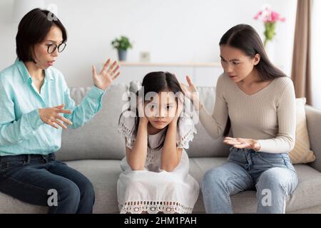 Malheureuse fille asiatique couvrant les oreilles tandis que la mère et la grand-mère en colère la collusion à la maison.Concept de problèmes familiaux Banque D'Images