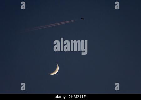 Gros plan de la lune de cire et d'un avion passant à proximité, laissant un contrail qui est illuminé par le soleil couchant - - prise de vue en début de soirée agai Banque D'Images