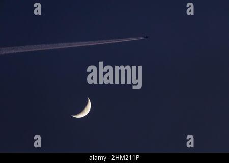 Gros plan de la lune de cire et d'un avion passant à proximité, laissant un contrail qui est illuminé par le soleil couchant - - prise de vue en début de soirée agai Banque D'Images